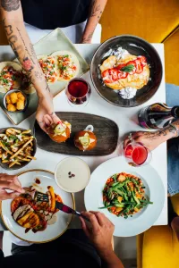 overhead shot of plates of colorful food. 3 people’s hands are seen holding food. 