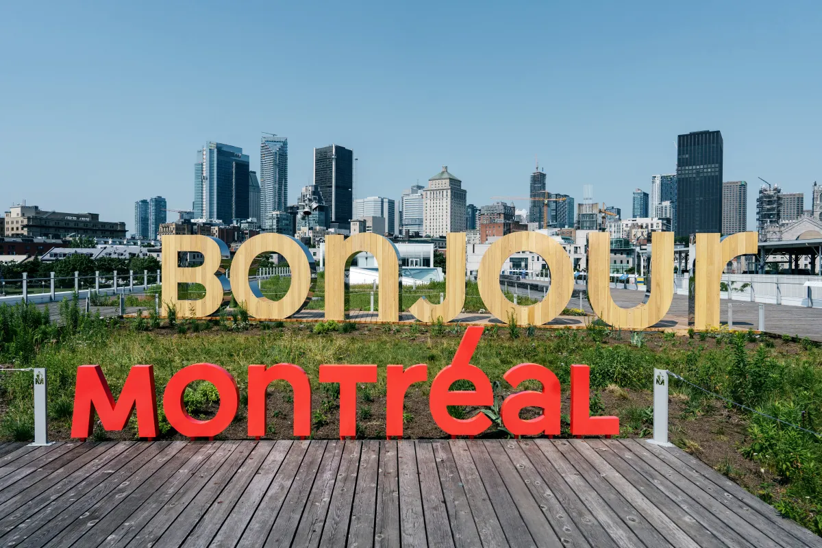 City Of Montreal day time skyline. The words Tourisme/ Montréal/Montre’al written over it. The word bonjour appears made of pine in foreground